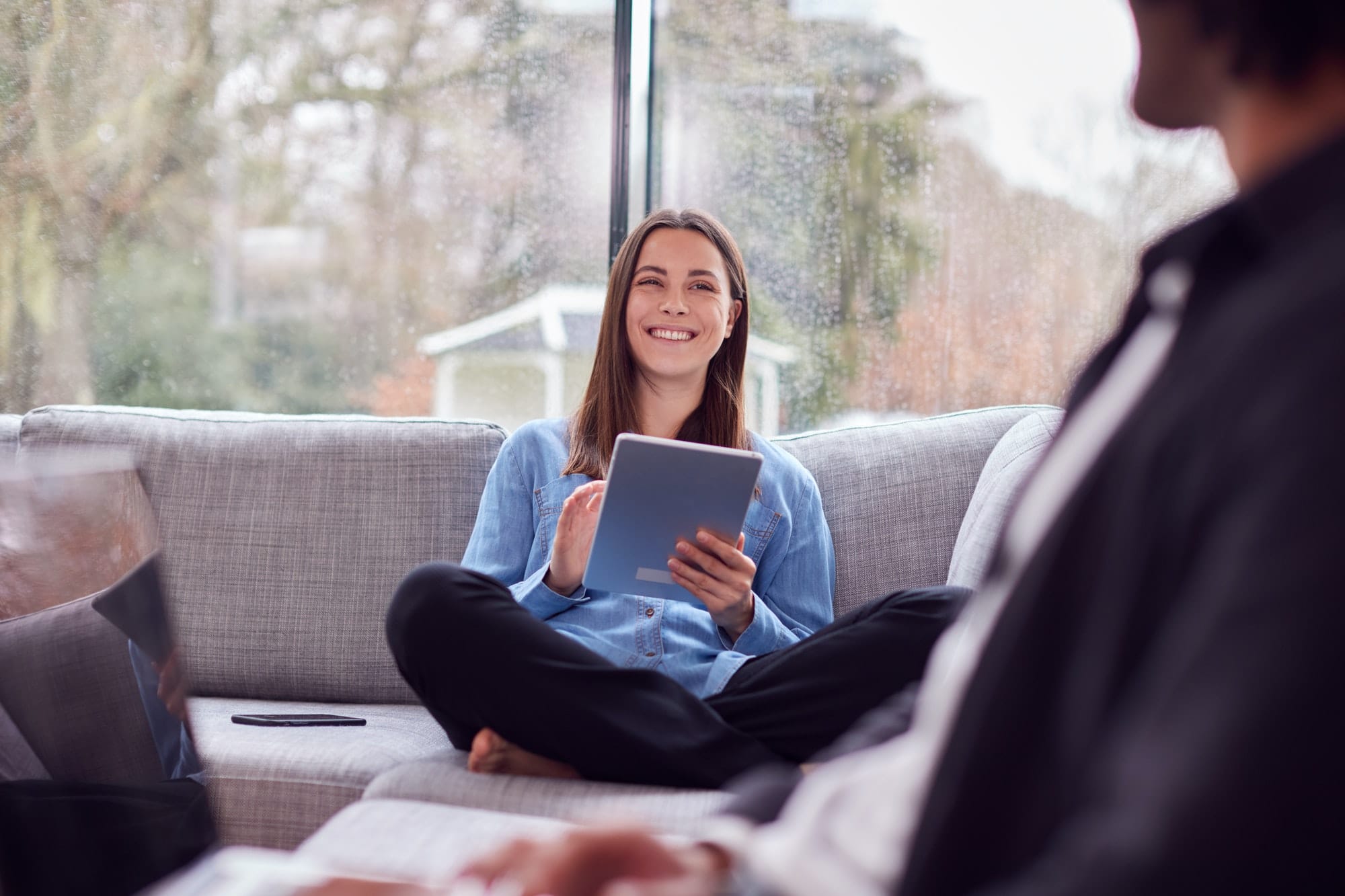 Relaxed Young Couple At Home Sitting On Sofa Using Digital Tablet And Reading Book Relaxed Young Couple At Home Sitting On Sofa Using Digital Tablet And Reading Book