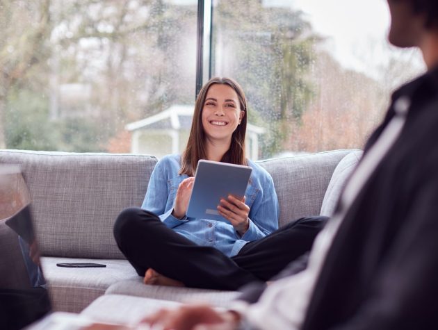 Relaxed Young Couple At Home Sitting On Sofa Using Digital Tablet And Reading Book Relaxed Young Couple At Home Sitting On Sofa Using Digital Tablet And Reading Book